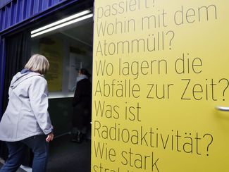 Bürgerin betritt Ausstellungscontainer, an der Tür sind Fragen zum Thema Atommüll angeschlagen.